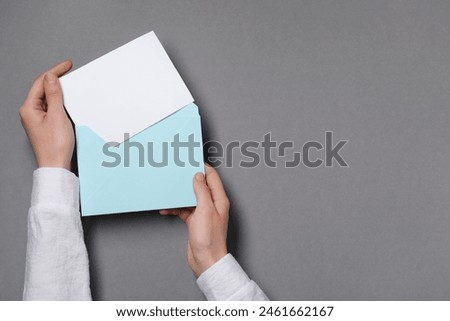 Woman taking card out of letter envelope at grey table, top view. Space for text