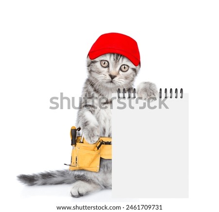 Funny cat wearing red cap and toolbelt shows blank notepad.  Isolated on white background Royalty-Free Stock Photo #2461709731