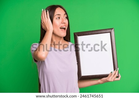 young pretty woman feeling happy, excited and surprised with an empty blank picture frame
