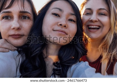 A group of young attractive multiethnic women take selfies and laugh outdoors. Smiling girls of different races have fun and take pictures in nature. Beautiful scenery and sunset.