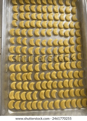 The picture shows a tray of yellow raw crescent cookies neatly arranged in a cake pan. Each piece of cake is half-moon shaped and looks freshly made focus only on the pan full of crescent cookies.