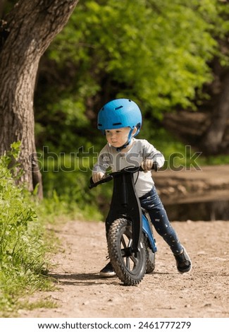 A little boy riding a balance bike in the countryside. Child with a clinging bicycle in a nature park.