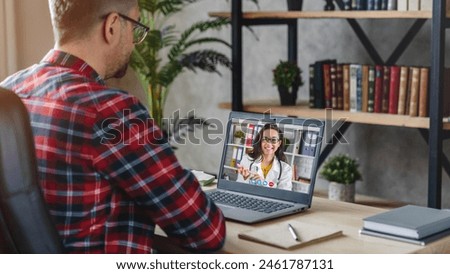 Back view of adult man using laptop for online video zoom call consultation with female doctor therapist while staying sitting at home. Patient doctor online consultation. Royalty-Free Stock Photo #2461787131