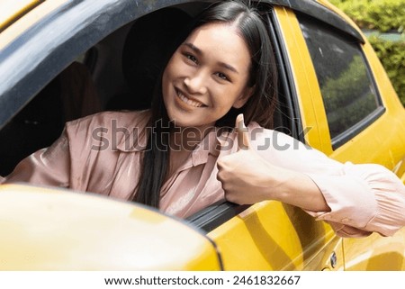 Happy smiling and relaxed woman driver drives with accepting thumb up, concept image for low gasoline price, good traffic condition, new car, passing driver license, taxi app, Right-side driving Royalty-Free Stock Photo #2461832667