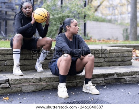 Two female friends sitting outdoors with basketball