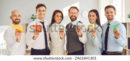 Portrait of happy smiling business people with paper planes in hands standing in office in a row and looking cheerful at camera. Team work, successful cooperation and business idea concept. Banner.