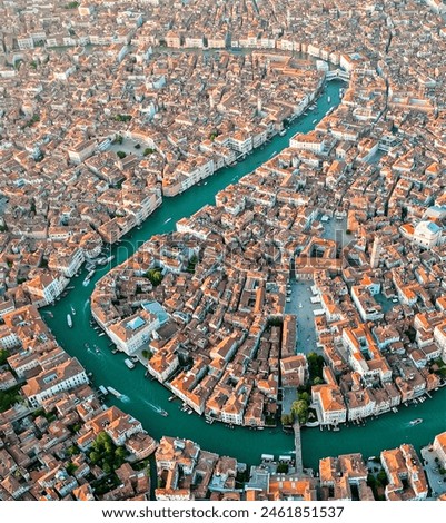 Aerial view of a dense cityscape with teal waterways, reddish-brown rooftops, and no visible green spaces, reflecting a historic or coastal European city at dawn or dusk.