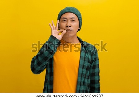 an Asian man, dressed in a casual shirt and wearing a beanie hat, is gesturing for silence by mimicking a zipped mouth, indicating a promise to keep someones secret safe, Isolated on Yellow background
