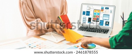 Cropped image of interior designer chooses color from color swatches while laptop displayed UI and UX designs for mobiles app and website. Creative design and business concept. Variegated.