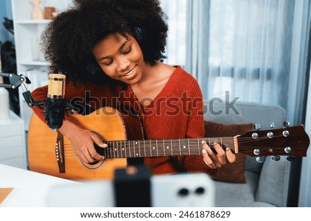 Host channel of beautiful African woman influencer singing with playing guitar in broadcast studio on smartphone. Time slot of music blogger on live social media. Concept of audio creator. Tastemaker.