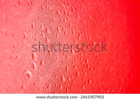 The photo shows a close-up of a surface covered with water droplets with a red background. The drops are arranged randomly and have different sizes, creating an interesting texture and rich picture. 