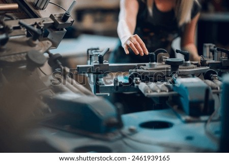 Close up of a female professional graphic technician's hands manipulating silkscreen printing machine at printing shop. Cropped picture of unrecognizable print shop expert operating silkscreen machine
