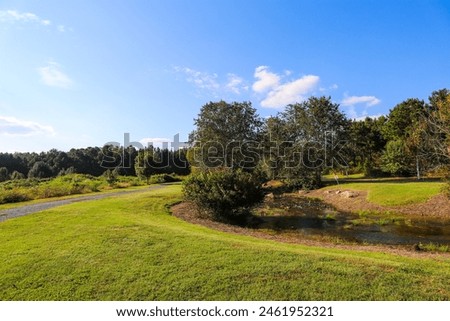 a stunning sunny day in the park with lush green and autumn colored trees, vast green grass and a running river with blue sky and powerful clouds at Garrard Landing Park in Alpharetta Georgia USA	