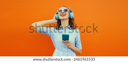 Portrait of happy smiling young woman listening to music in headphones with smartphone on bright orange background