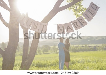 a guy and a girl of Asian nationality Kyrgyz in nature, against the backdrop of the mountains. holding a sign, banner newlyweds, newlyweds