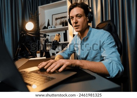 Host channel smart broadcaster talking on live social media application searching on laptop, broadcasting streamer wearing headphone using mic at modern home office studio in warm lighting. Pecuniary.