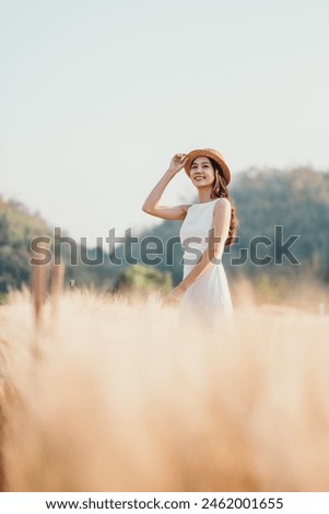 A woman is standing in a field of tall grass, wearing a white dress and a straw hat. She is smiling and looking up at the sky. Concept of freedom and relaxation, as the woman is enjoying the outdoors