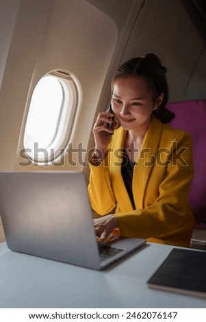 Young woman, business woman in a yellow suit is using a smartphone to communicate with customers and Friends on plane and laptop with Wi-Fi internet connection on plane. Travel concept.