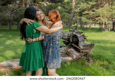 Three women share a heartfelt hug in a sunlit forest, expressing joy and friendship surrounded by nature. Royalty-Free Stock Photo #2462083467