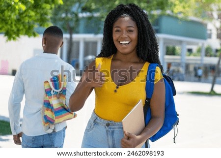Successful black female student showing thumb up outdoor in summer in city