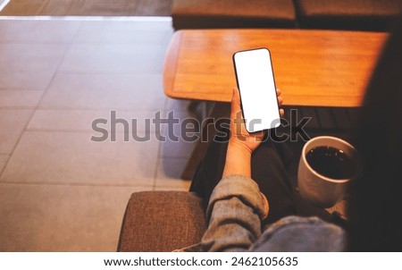 Mockup image of a woman holding mobile phone with blank desktop screen while drinking coffee in cafe