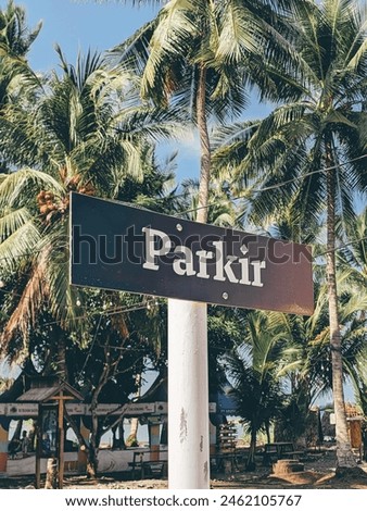 A colorful parking sign stands amidst a row of lush palm trees on a pristine tropical beach
