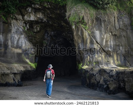 Man walking to the entrance of Muriwai cave. Muriwai Beach in summer. Auckland.  Royalty-Free Stock Photo #2462121813