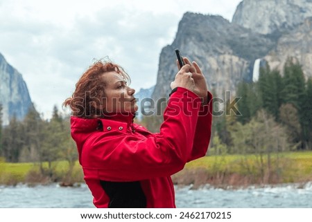 Young woman takes pictures of a natural landscape in Yosemite Park, California with a smartphone camera. Yosemite Falls in Springtime. Scenic view of rocky mountains against sky