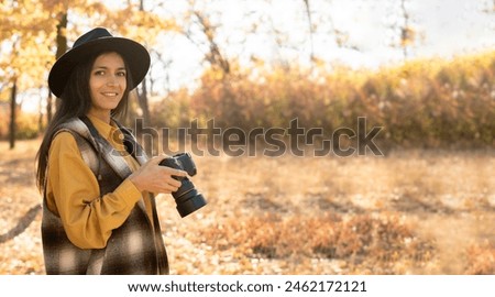 A Caucasian photographer in a hat stands in the autumn forest, creating stunning shots. looks at the camera and smiles. Banner. copy space.
