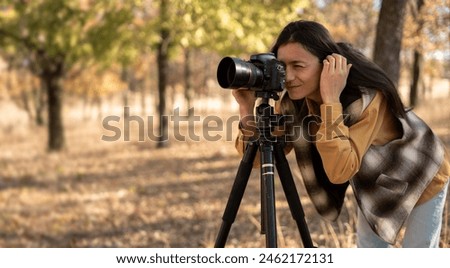 beautiful Caucasian woman doing a photo shoot in the autumn forest. Professional photographer photographing a landscape on a sunny day using a camera and a tripod in search of a beautiful angle.