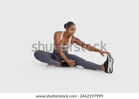 African American woman is engaged in a stretching exercise on the floor, extending her arms and legs to improve flexibility and muscle strength, white background Royalty-Free Stock Photo #2462197999