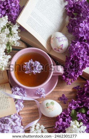 Easter and eggs, a cup of tea and lilac flowers, spring still life. Translation of what is written on the egg: Christ is Risen.
