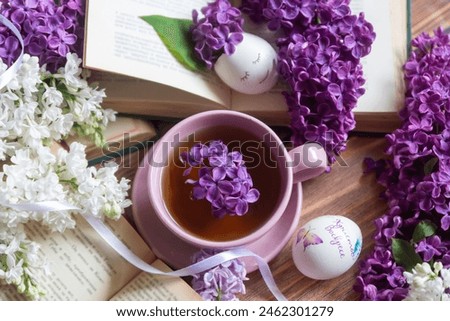 Easter and eggs, a cup of tea and lilac flowers, spring still life. Translation of what is written on the egg: Christ is Risen.