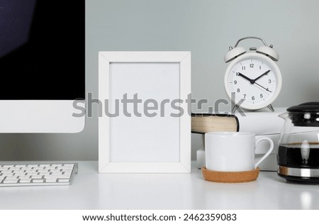 Empty picture frame on table in workspace with computer and coffee cup