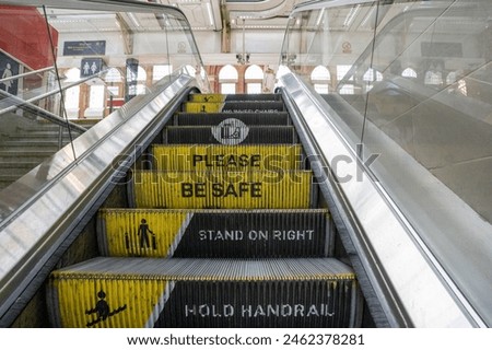 Escalator at the train station with step riser messaging, please be safe, stand on right and hold handrail. Safety sign and warning.