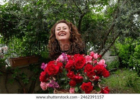 A happy, smiling woman holding a basket of red and pink roses in her lap.