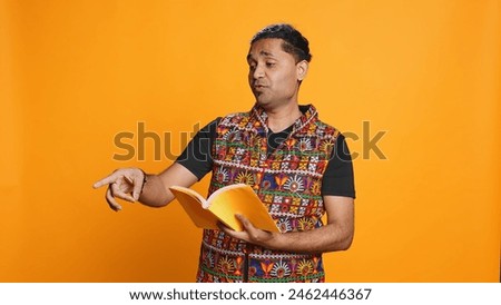Joyous indian teacher reading book for pupils during class, isolated over studio background. Cheerful man holding novel, telling story to kindergarten kids, teaching them, camera B