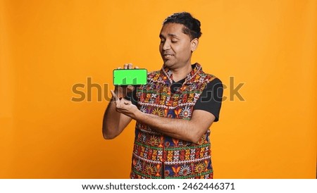Content creator in traditional clothing recommending isolated screen phone, studio backdrop. Indian man reviewing copy space mockup smartphone device for online tech channel, camera B