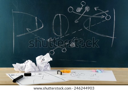 Table with sheets of paper and blackboard with scheme basketball game on background