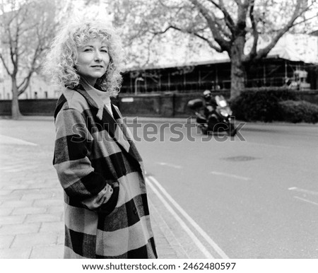 Monochrome portrait of curly woman standing beside a road in London. There is traffic behind her and she is looking at camera. Film analogue image made with medium format camera.