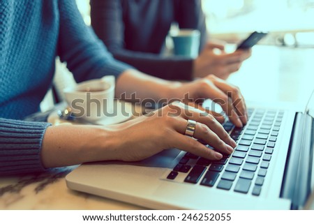 Female hands typing on the laptop keyboard in cafe. Toned picture