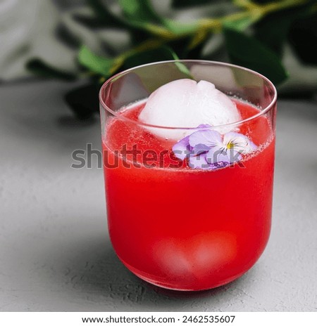 Elegant watermelon cocktail adorned with an ice sphere and delicate pansy, perfect for summer refreshment