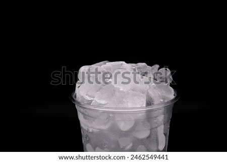 Ice and plastic cups for cold drink in summer. Close-up ice cube texture in a plastic cup with black background and space for text. For beverages, iced coffee, takeaway drinks, and food delivery.  Royalty-Free Stock Photo #2462549441