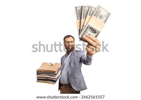 Man with a pile of folded clothes smiling at camera and holding money isolated on a white background