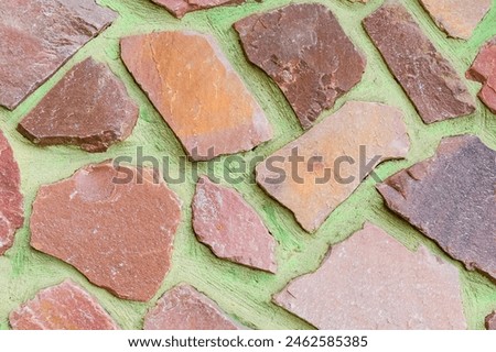 It is view of colorful stones on green background. Its the close up view of mosaic stone wall of building. It is photo of multicolored stone tile floor