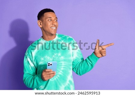 Photo of attractive funny guy wear teal sweatshirt typing modern gadget showing emtpy space isolated purple color background