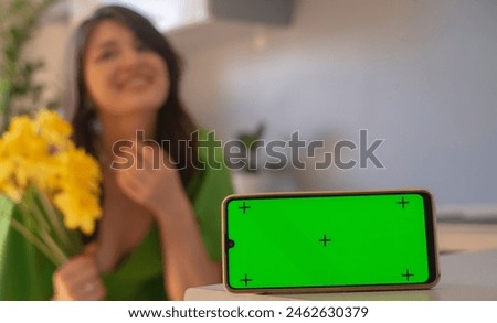 A woman enjoys the aroma of a bouquet of daffodils. Congratulations on the Day of Family Love and Loyalty and Mother's Day. Phone with green screen in the foreground.