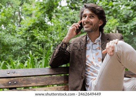 View of a young man with smartphone sitting on a bench at daytime in a green park in the city. High quality photo. 