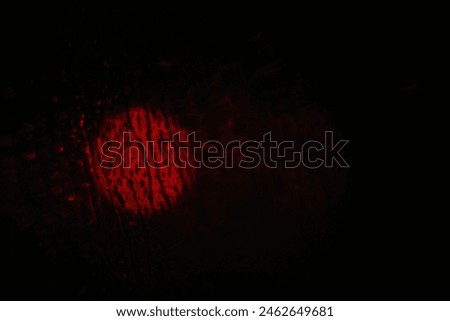 A circular blurred red light from behind a wet car window under a pitch black night sky in the rain.