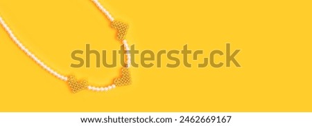 Banner with beads made from imitation pearls with pendants in a heart shape on a yellow background. 